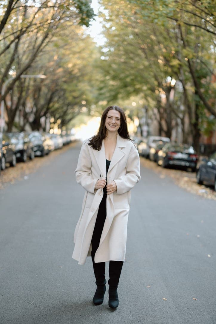 Emily Hyeamang in a cream coat on a tree-lined street
